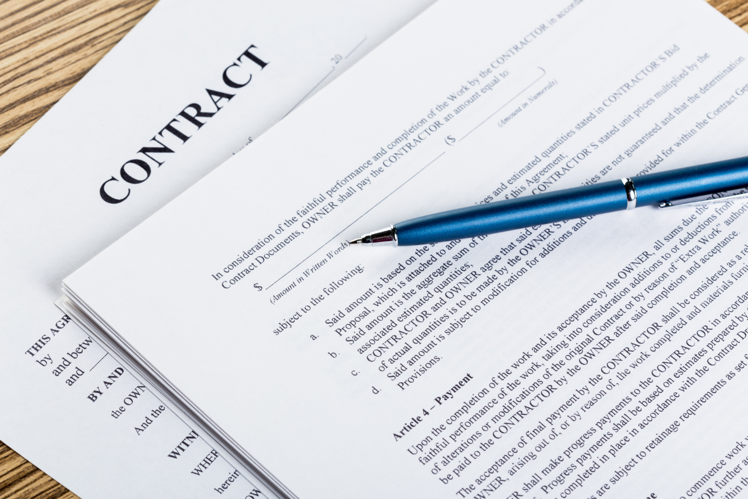 Close-up shot of a stack of contract paperwork with a blue pen on top of a wooden table.