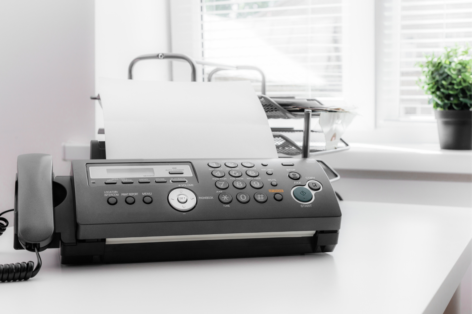 Fax Machine Sitting on Desk A black fax machine on a white office desk.