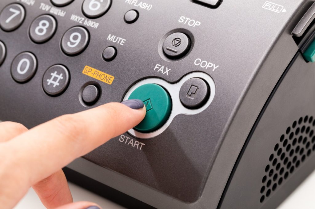 Close-up of a person pressing the green start button on a fax machine, highlighting the device's controls and functionality for sending faxes