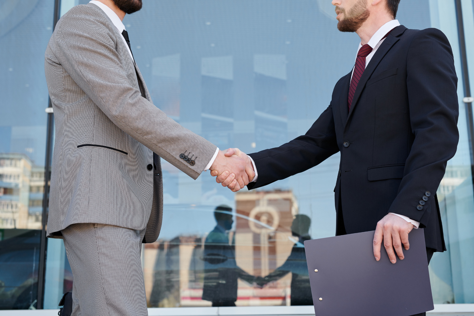 Two businessmen shake hands in front of an office building.